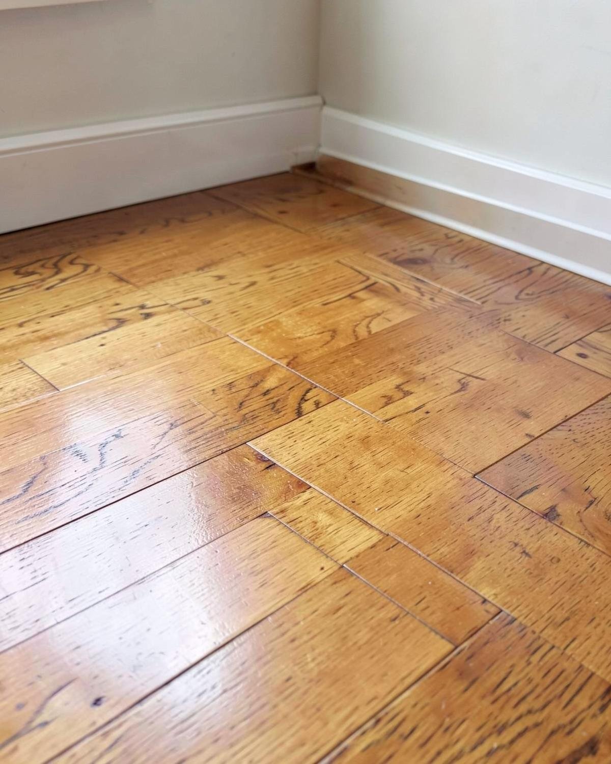 Refinished hardwood flooring with a glossy amber finish in the corner of a room